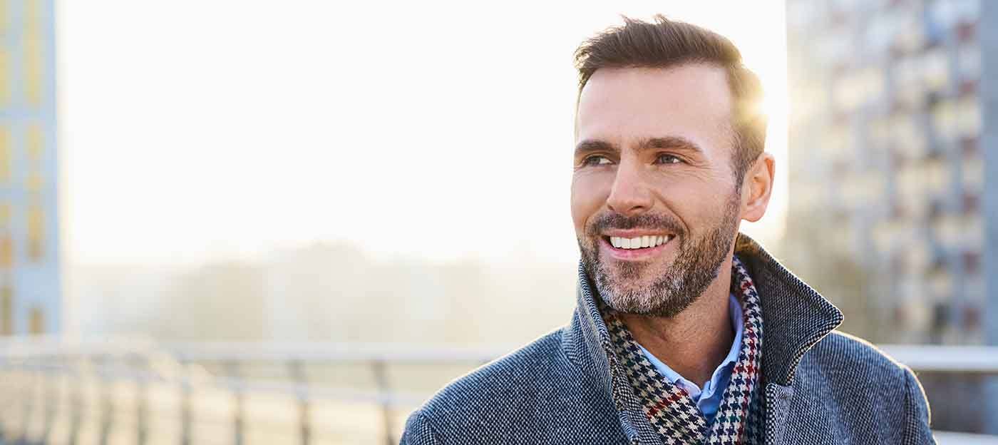 A smiling man standing outdoors during a sunny day