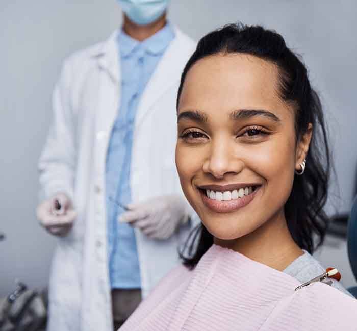 A smiling woman sitting in a dentist’s chair while a dentist stands in the background