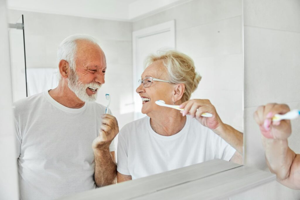 An older man and woman brushing their teeth in front of a mirror